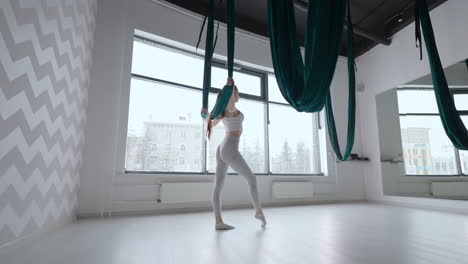 Attractive-fitness-trainer-doing-antigravity-aerial-flying-yoga-exercises-in-green-hammock.-Young-flexible-woman-practice-in-aero-stretching-swing-in-fitness-club.-Female-fitness-yoga-routine-concept